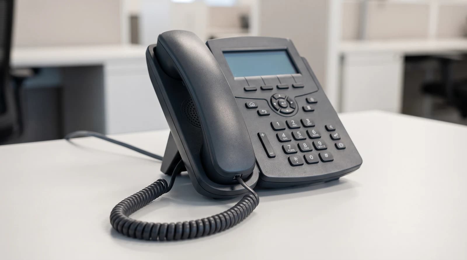 A black IP desk phone with a corded handset on an office desk