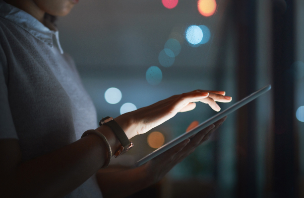 Woman in dark room whose hand illuminated by tablet screen